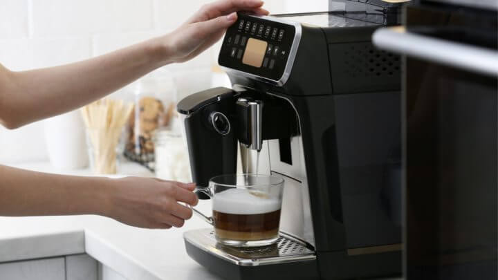 Pessoa com mão em máquina de café e segurando uma caneca com café