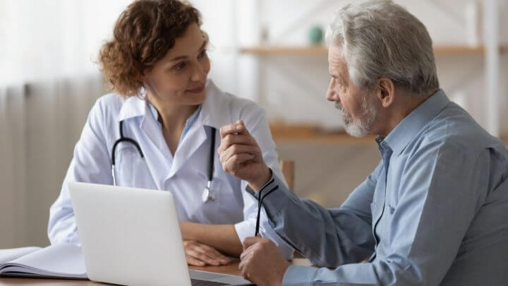 Médica e senhor sentados em frente a computador conversando