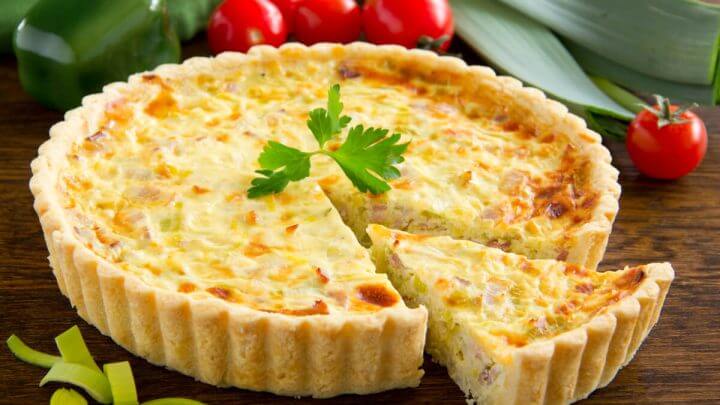 Quiche em cima de uma mesa de madeira com um pedaço cortado