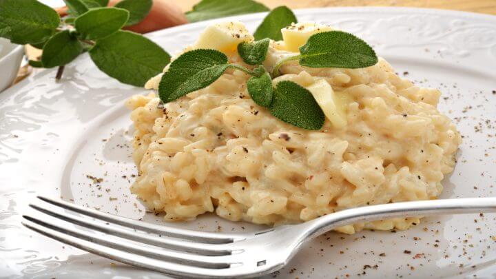 Arroz cremoso com folha verde em cima em prato branco com garfo ao lado