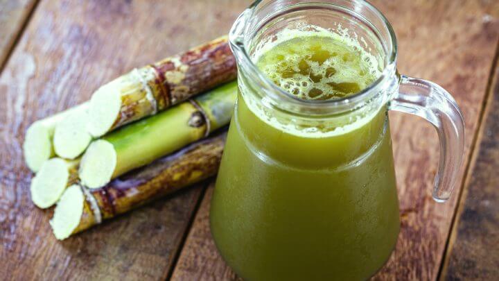 Caldo de cana em jarra de vidro transparente sob mesa de madeira com alguns pedaços de cana-de-açúcar