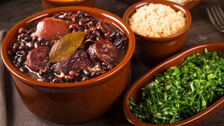 Feijoada em panela de barro ao lado de recipiente com couve e farofa