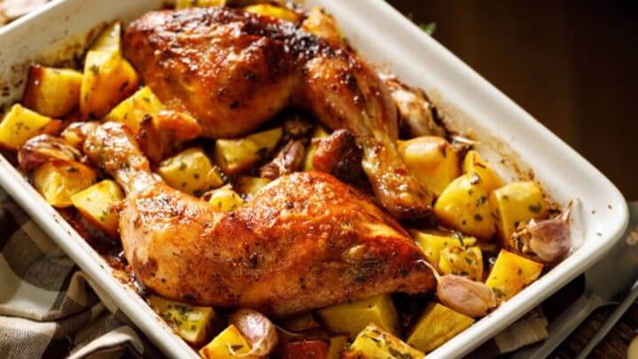 Travessa branca com coxas de frango, batatas e alho