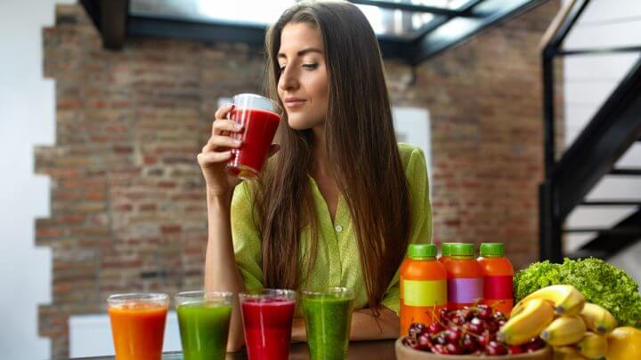 Mulher tomando suco encostada em mesa com frutas e sucos