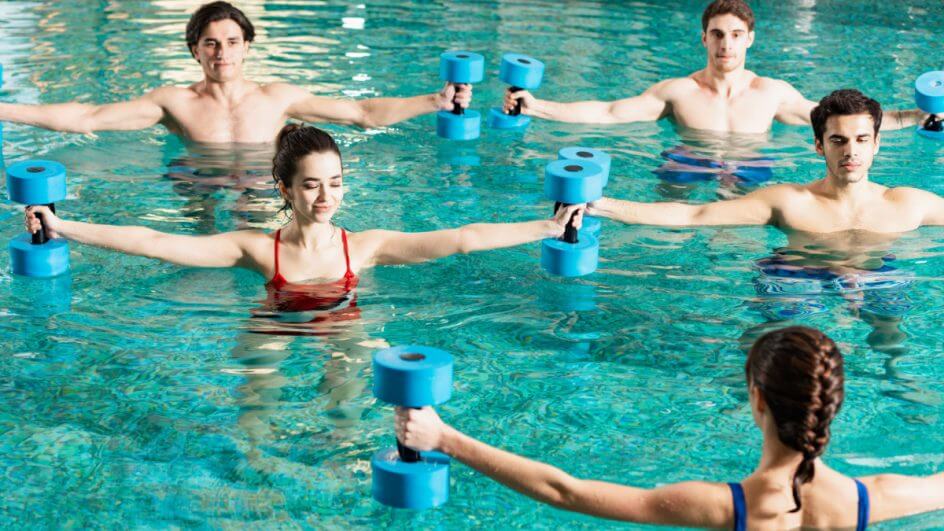 Pessoas em piscina fazendo hidroginástica com peso nas mãos