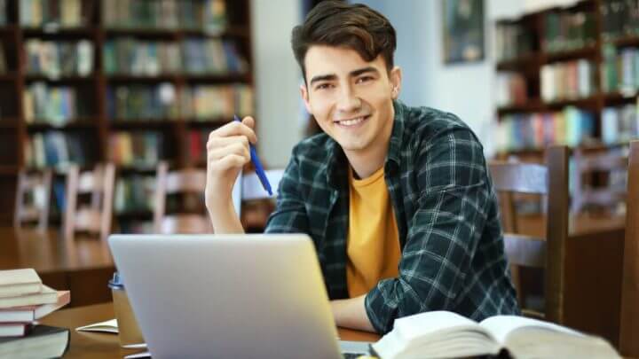 Adolescente vestindo blusa xadrez sentado estudando em frente a um notebook