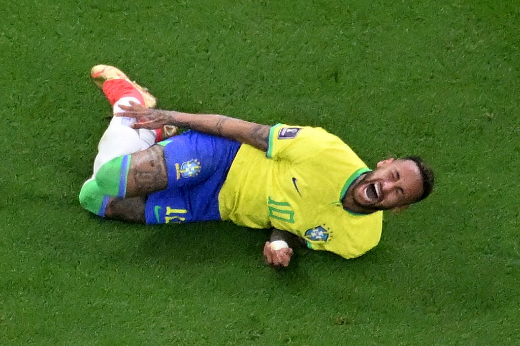 Neymar caído no chão com a mão no tornozelo direito