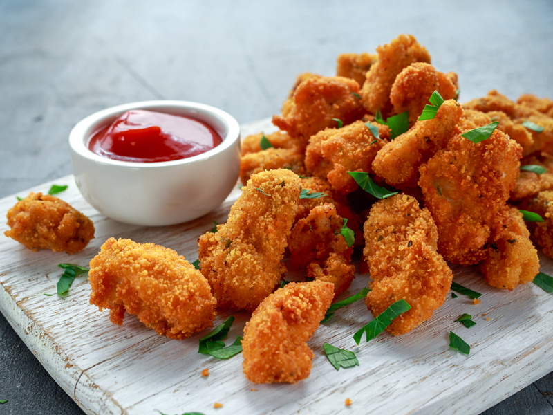 Nuggets em cima de tábua branca salpicado com salsinha e porte de ketchup ao lado
