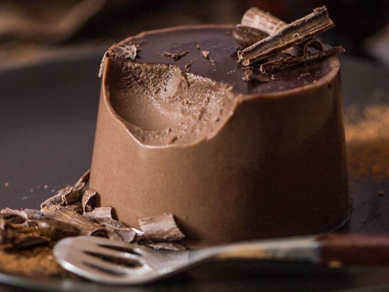 Flan de chocolate com pedaços de chocolate em cima e uma colher ao lado