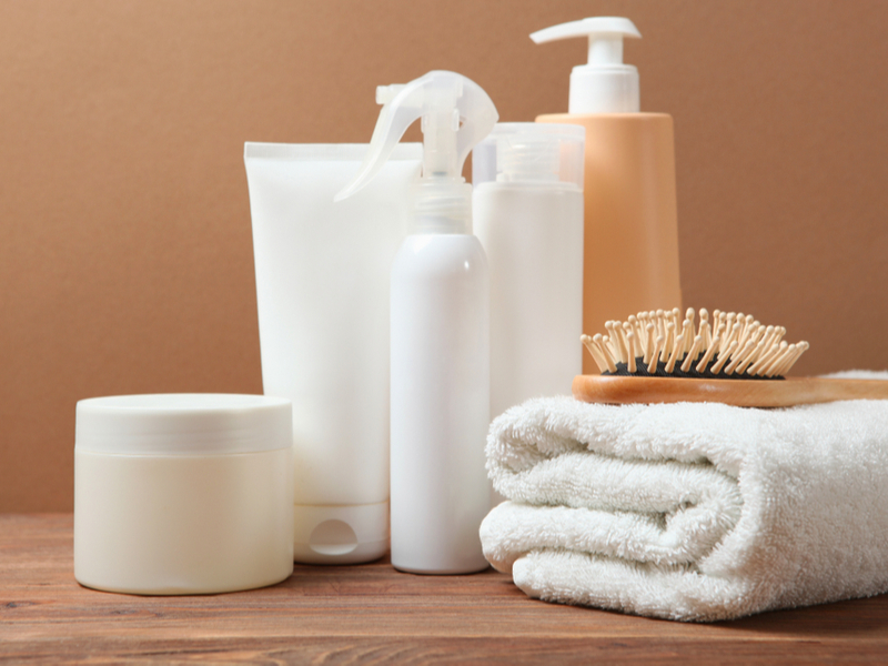 Produtos em spray e em creme, escova de cabelo e toalha branca em cima da mesa de madeira