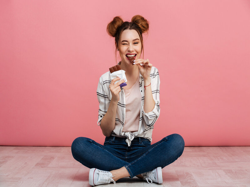 Mulher sentada, sorrindo e comendo chocolate