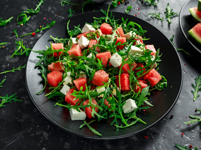 Salada de rúcula com melancia e queijo feta em cima de um prato preto