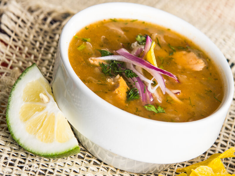 Encebollado de pescado em um recipiente branco decorado com cebola roxa e coentro