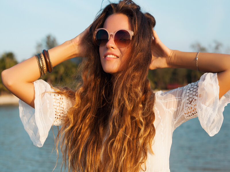 Mulher sorrindo, usando óculos e com as mãos no cabelo