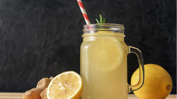 Copo com canudo e suco de limão, limões-siciliano e gengibre ao lado