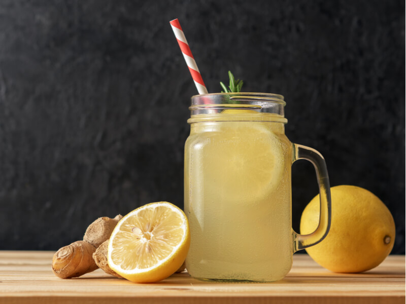 Copo com canudo e suco de limão, limões-siciliano e gengibre ao lado