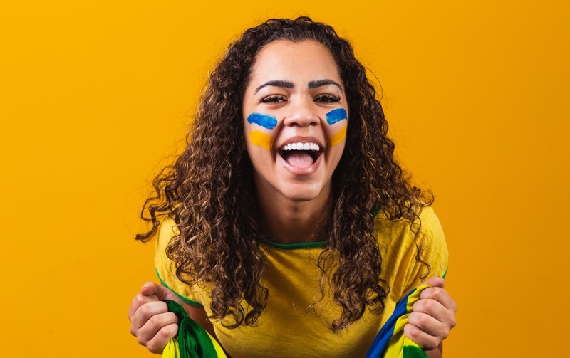 Mulher vibrando com bandeira do Brasil na mão e o rosto pintado de azul e amarelo
