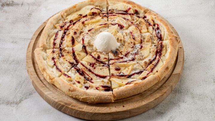 Pizza com pedaços de maçã, bola de sorvete e calda em cima de uma mesa branca