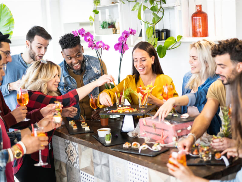 Grupo de amigos reunidos na cozinha e com diversos alimentos em cima da mesa
