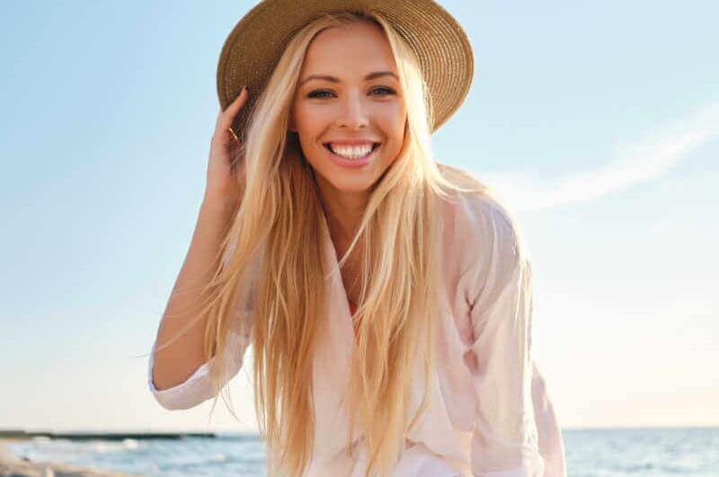 Mulher feliz usando chapéu e uma praia ao fundo