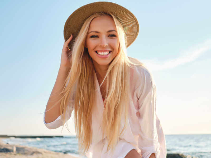 Mulher feliz usando chapéu e uma praia ao fundo