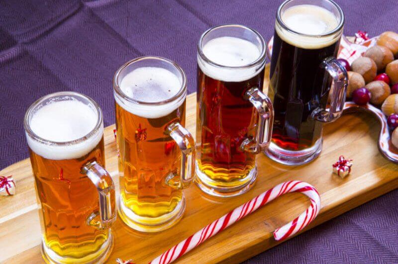 Quatro copos cheios com cerveja e decoração natalina ao redor em cima da tábua de madeira