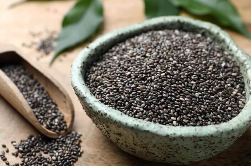 Sementes de chia dentro do bowl verde e espalhadas ao redor em cima da mesa