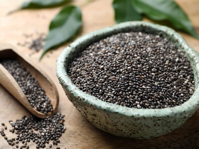 Sementes de chia dentro do bowl verde e espalhadas ao redor em cima da mesa