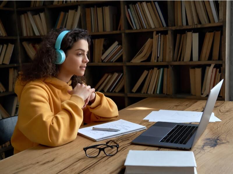 Menina sentada com o notebook aberto e cadernos e lápis em cima da mesa