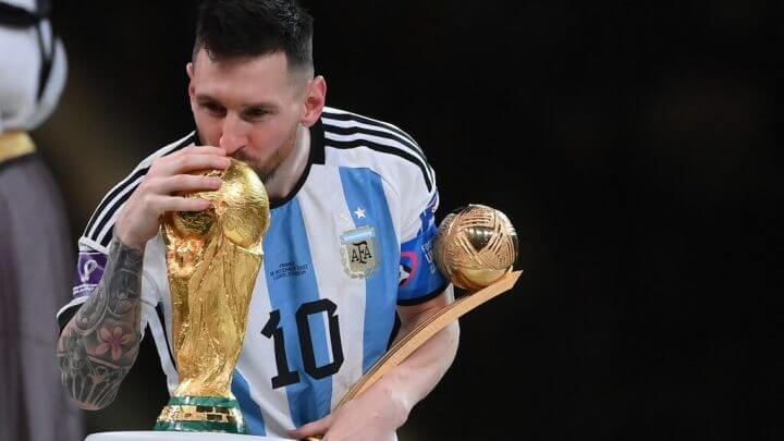 Lionel Messi segurando troféu de melhor jogador da Copa do Mundo e beijando a taça do mundial