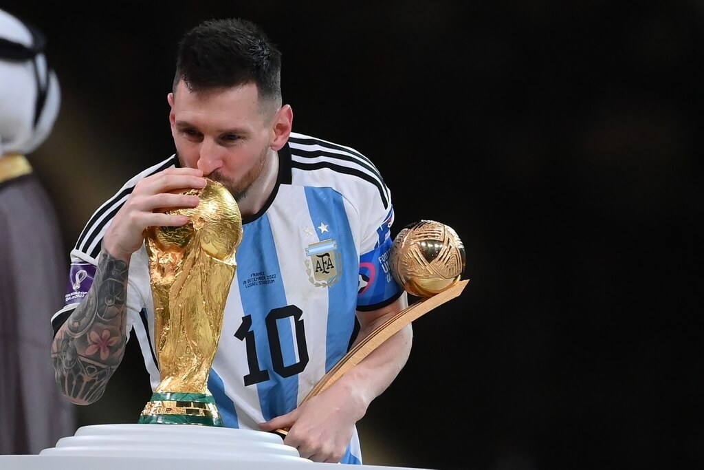 Lionel Messi segurando troféu de melhor jogador da Copa do Mundo e beijando a taça do mundial