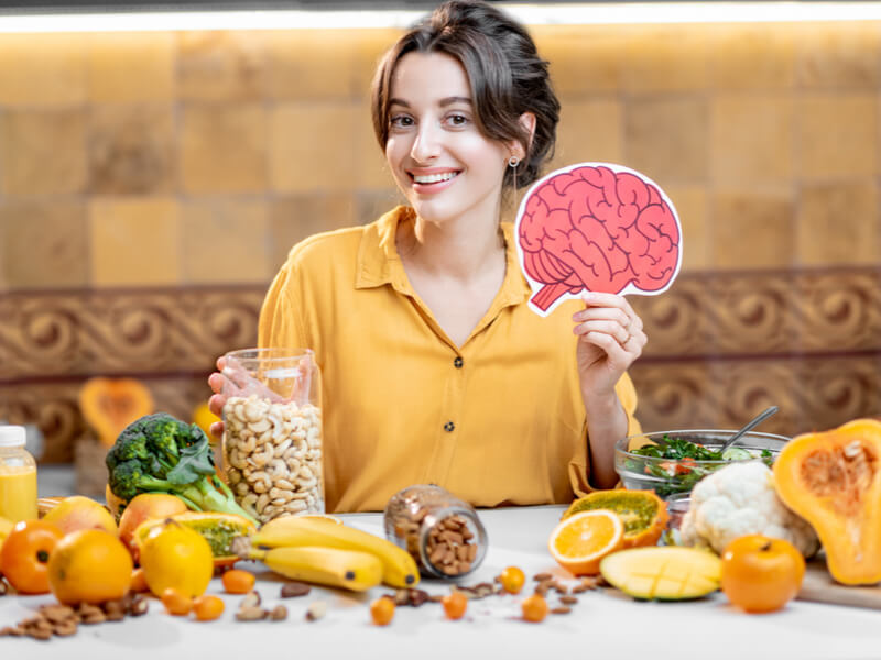Mulher sorrindo segurando o desenho de um cérebro com uma mesa com alimentos
