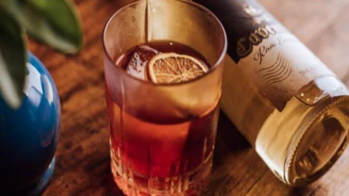 Copo com drink Kingston Negroni e garrafa de rum ao lado