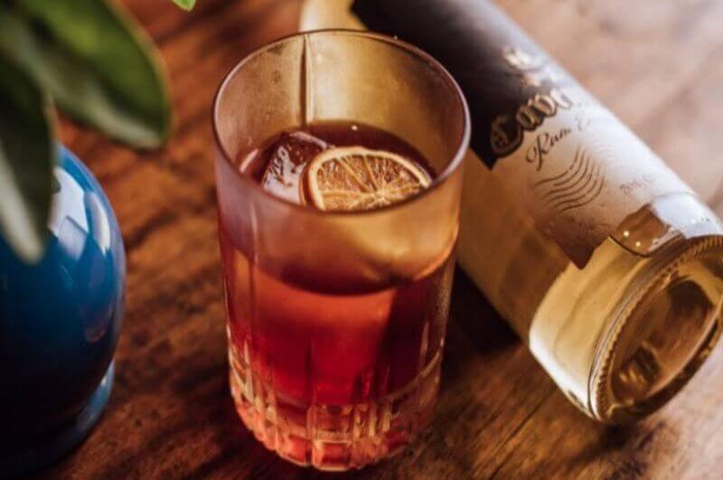 Copo com drink Kingston Negroni e garrafa de rum ao lado