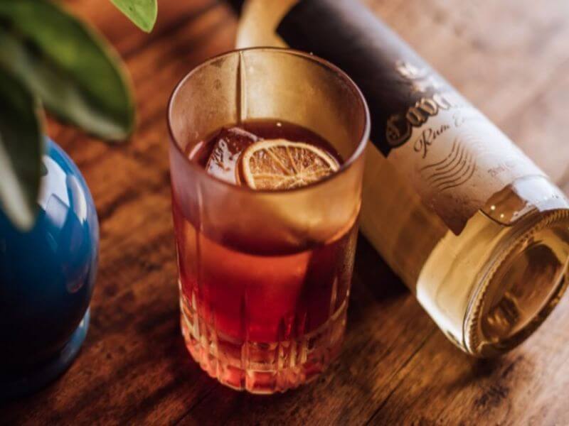 Copo com drink Kingston Negroni e garrafa de rum ao lado