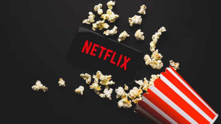 Balde de pipoca caído e celular com logo da Netflix no fundo preto