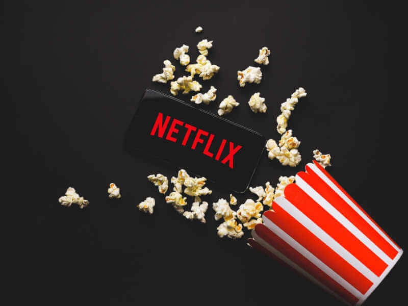 Balde de pipoca caído e celular com logo da Netflix no fundo preto