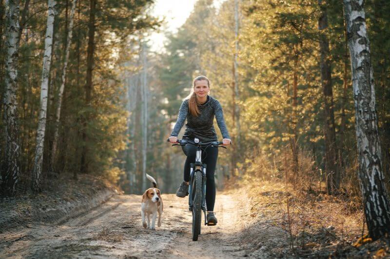 Mulher pedalando ao ar livre com cachorro do lado