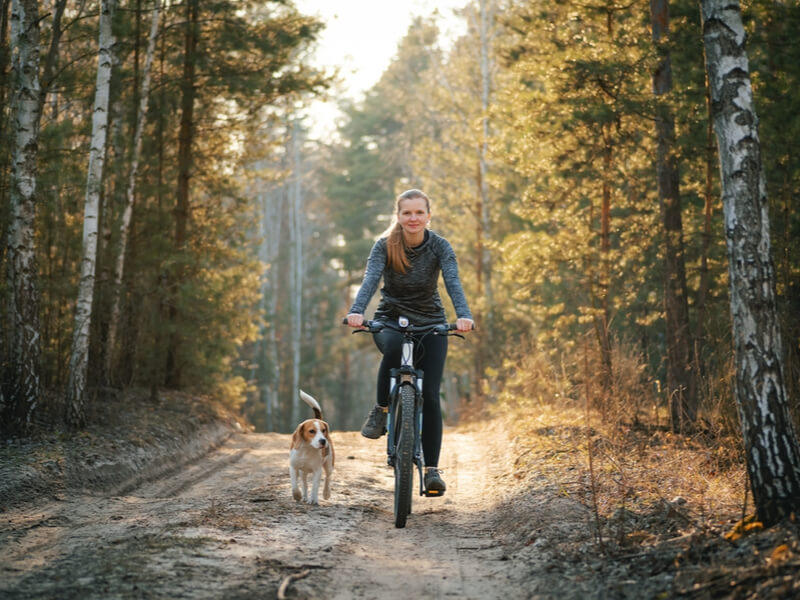 Mulher pedalando ao ar livre com cachorro do lado