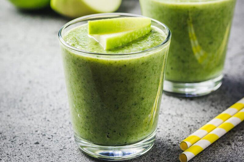 Copo de vidro com suco verde decorado com pedaço de maçã