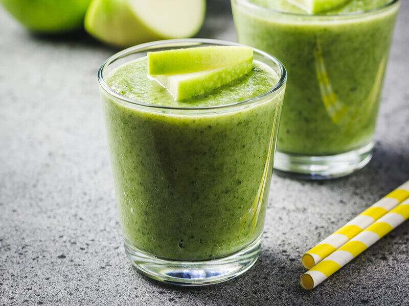 Copo de vidro com suco verde decorado com pedaço de maçã