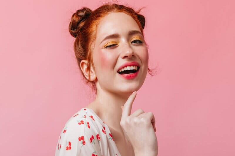 Mulher de maquiagem sorrindo com a mão no queixo