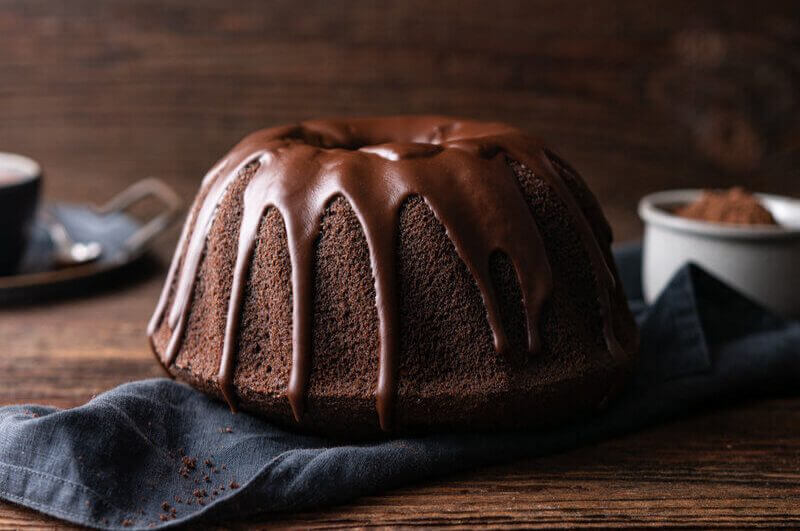 Mesa de madeira com um bolo de chocolate com cobertura em cima de um pano azul