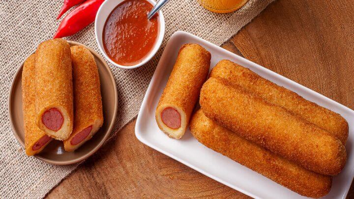 Enroladinhos de salsicha em cima de um prato branco com recipiente com molho ao lado