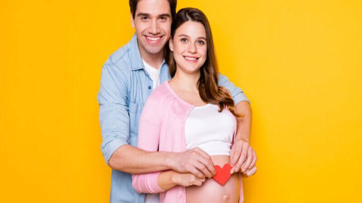 Homem abrançando uma mulher grávida com um coração na barriga