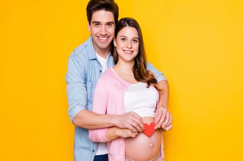 Homem abrançando uma mulher grávida com um coração na barriga