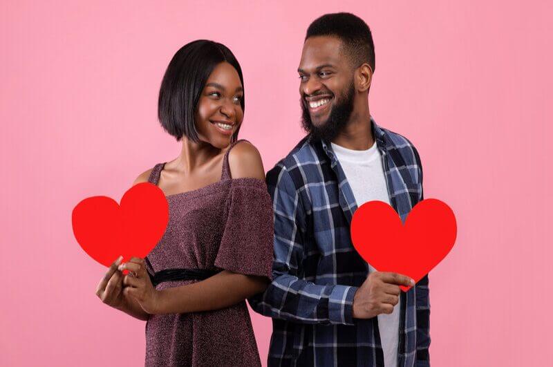 Homem e mulher em frente a um fundo rosa se olhando e segurando corações