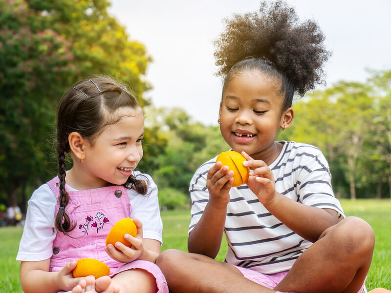 Duas meninas sentadas em um parque comendo laranja