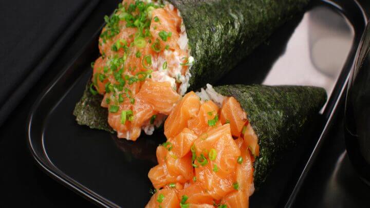 Dois temaki em cima de um prato preto decorado com salsinha e cebolinha picada