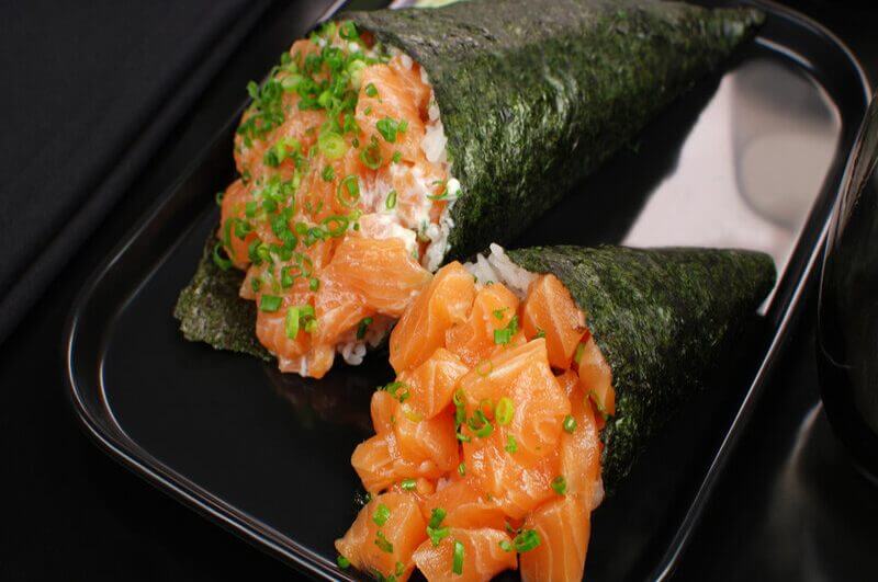 Dois temaki em cima de um prato preto decorado com salsinha e cebolinha picada